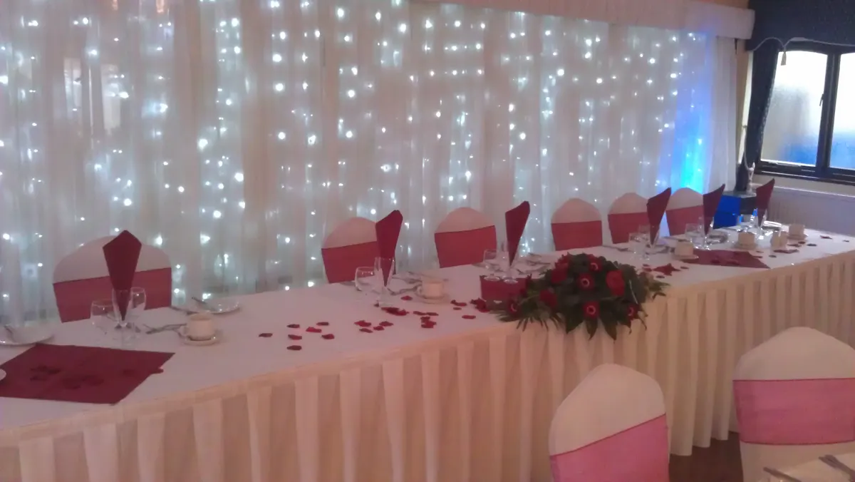 A decorated event table with pink chair sashes and a lit backdrop